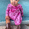 child, baby, pink_dress, cowboy_boots, porch, step, flowers, basket, outdoor, serious_expression, sitting, concrete, pavement, hair_buns, patterned_clothing, footwear, person, young_child, casual, daylight