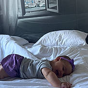 Kamila participe au concours pour gagner de l'argent avec cette photo : baby, bed, white_bed, pillow, purple_headband, purple_shorts, gray_shirt, smiling, happy, infant, indoor, window, curtain, harbor, boats, cityscape, soft_light, sleeping, child, portrait