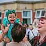 baby, child, adult, smiling, laughing, green_headwrap, patterned_dress, outdoor, people, happy, joyful, family, celebration, crowd, red_hair, woman, man, holding, fun, event