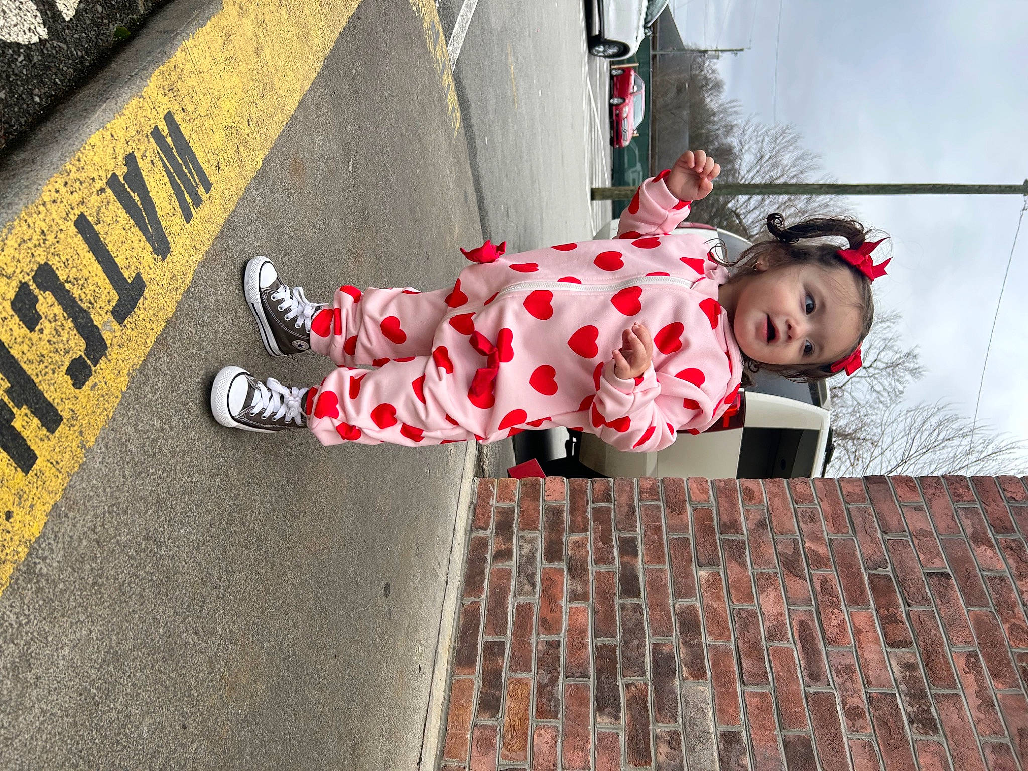 Jianna is registered to the contest to win money with this photo: asphalt, carmine, city, concrete, human_leg, logo, pattern, pedestrian, person, road, road_surface, shadow, sidewalk, sitting, sky, street, tints_and_shades, toddler, tree, wall