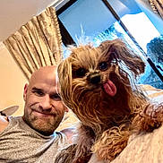 Chanel joined the competition — help win amazing prizes! man, dog, pet, smile, tongue_out, indoor, curtains, bed, window, happy, casual, person, furniture, home, animal, cute, companion, relaxed, portrait, light