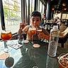 beverage, bottle, casual, child, coaster, curtain, drink, gesture, glass, happy, indoor, interior, light, napkin, peace_sign, people, restaurant, seated, table, window