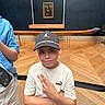 child, boy, museum, portrait, selfie, cap, baseball_cap, shirt, puma, smiling, face, person, artwork, mona_lisa, gallery, interior, wooden_floor, fashion, pose, tourist