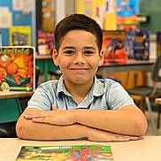 Mikael joined the competition — help win amazing prizes! arms_crossed, background_blur, boy, casual_clothing, child, classroom, desk, education, furniture, haircut, happy, indoor, learning, person, poster, school, short_sleeves, smiling, student, youth