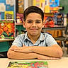 Mikael joined the competition — help win amazing prizes! arms_crossed, background_blur, boy, casual_clothing, child, classroom, desk, education, furniture, haircut, happy, indoor, learning, person, poster, school, short_sleeves, smiling, student, youth