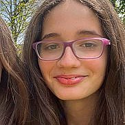 Eliana is registered to the contest to win money with this photo: girl, child, glasses, smile, long_hair, outdoor, nature, tree, sky, sunlight, face, portrait, young, casual, person, daylight, greenery, happy, head, fashion