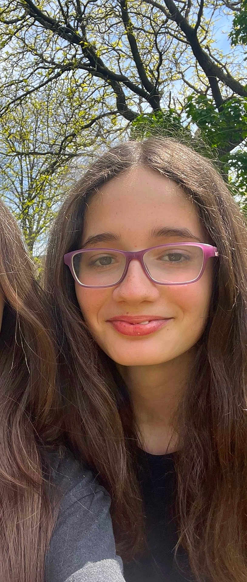 Eliana is registered to the contest to win money with this photo: girl, child, glasses, smile, long_hair, outdoor, nature, tree, sky, sunlight, face, portrait, young, casual, person, daylight, greenery, happy, head, fashion