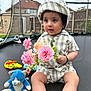 toddler, child, baby, striped_clothing, hat, flowers, pink_flowers, stuffed_toy, blue_cat, trampoline, outdoor, backyard, toys, sitting, curious, bracelet, daylight, fence, grass, house