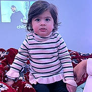 Rijak Kaur joined the competition — help win amazing prizes! child, toddler, striped_sweater, indoor, blanket, patterned_blanket, hand_holding, curly_hair, big_eyes, sitting, person, portrait, casual_clothing, young_child, cozy, soft_lighting, curious_expression, face, home, comfort