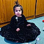 toddler, child, black_dress, sequins, carpet, metal_dishes, spoon, wooden_cabinet, indoor, sitting, curious, hair_topknot, barefoot, floor, young_child, portrait, playing, home, furniture, expression