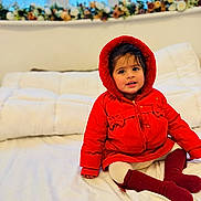 Rijak Kaur joined the competition — help win amazing prizes! toddler, child, red_jacket, hood, boots, white_bed, flower_arrangement, window, indoors, cute, smiling, sitting, warm_clothing, face, person, home, soft_lighting, cozy, curious, young_child
