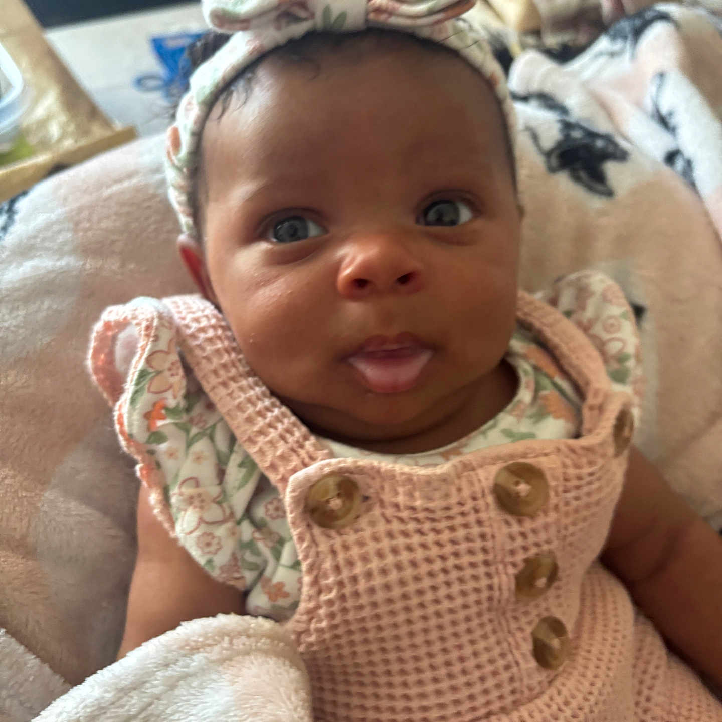 Atlantis is registered to the contest to win money with this photo: baby, infant, headband, pink_outfit, blanket, tongue_out, closeup, cute, child, indoors, expression, person, soft_texture, buttoned_clothing, fabric, cozy, portrait, newborn, face, wearing