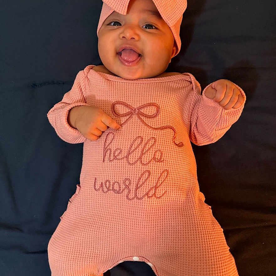 Winta joined the competition — help win amazing prizes! baby, infant, smiling, headband, bow, peach, outfit, clothing, lying_down, happy, child, cute, portrait, indoors, person, text_on_clothing, fabric, hands, feet, face