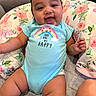 Winta is registered to the contest to win money with this photo: baby, blue_onesie, child, chubby, cozy, cute, face, floral_cushion, hand, happy, indoors, infant, legs, person, portrait, rainbow, sitting, skin, smiling, soft_fabric