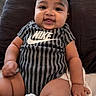baby, bed, bow, child, chubby_cheeks, cute, hand, happy, headband, indoor, infant, legs, onesie, person, pillow, sitting, skin, smiling, soft_lighting, striped_clothing