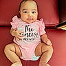 baby, child, chubby_cheeks, comfortable, cute, eyes, face, feet, hair, hands, happy, indoor, infant, legs, pink_onesie, portrait, red_couch, seated, smiling, text_on_clothing