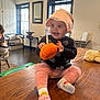 baby, child, smiling, sitting, hat, bonnet, toy, pumpkin, indoor, table, wood, pink_pants, socks, face, person, window, furniture, room, happy, cozy