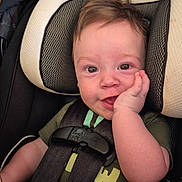 Lucas is registered to the contest to win money with this photo: baby, child, car_seat, smile, happy, infant, seatbelt, toddler, face, hand, hair, clothing, green_shirt, safety, cute, portrait, indoors, seat, closeup, person