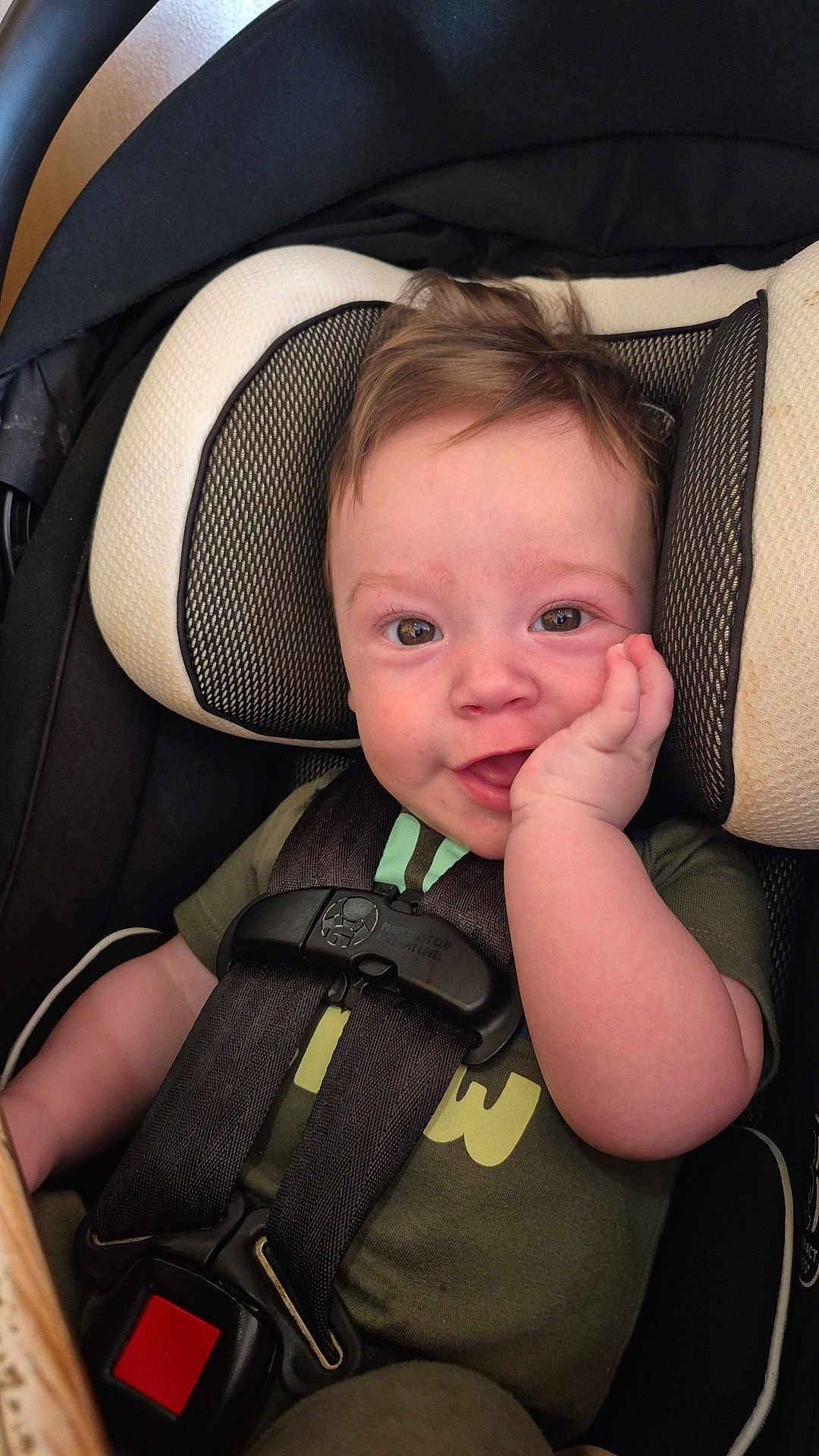 Lucas is registered to the contest to win money with this photo: baby, child, car_seat, smile, happy, infant, seatbelt, toddler, face, hand, hair, clothing, green_shirt, safety, cute, portrait, indoors, seat, closeup, person