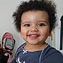 child, toddler, smile, curly_hair, indoor, face, happy, clothing, person, baby, table, furniture, stroller, pink, white, eyes, mouth, skin, head, cute