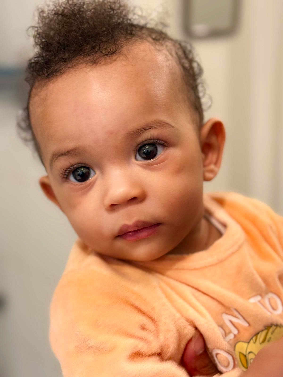 Kingston a rejoint le concours — aidez-le/la à gagner de superbes lots ! adorable, baby, child, close_up, curly_hair, cute, expression, face, head, indoors, infant, large_eyes, looking_away, peach_clothing, person, portrait, skin, small_hand, soft_light, young_child