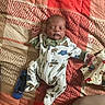 baby, sleeping, onesie, blanket, remote_control, pillow, teddy_bear_pattern, bedroom, infant, cozy, patterned, child, peaceful, cute, resting, home, soft, fabric, person, relaxing