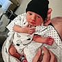 Theo joined the competition — help win amazing prizes! newborn, baby, infant, black_hat, white_blanket, patterned_onesie, hand, cradle, indoor, bedroom, polka_dot, cute, small, sleepwear, skin, face, person, holding, resting, cozy