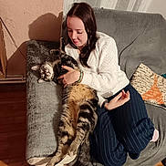 Sony participe au concours pour gagner de l'argent avec cette photo : woman, cat, couch, indoor, cozy, white_sweater, tabby_cat, relaxed, affection, pillow, striped_pants, wooden_floor, homedecor, seated, pet, casual, smiling, long_hair, grey_fabric, warm_lighting
