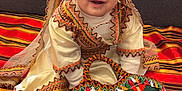 Ayla a rejoint le concours — aidez-le/la à gagner de superbes lots ! child, baby, infant, toddler, smiling, traditional_clothing, ethnic_costume, couch, blanket, woven_bag, colorful, sitting, indoor, portrait, happy, headwear, tassel, fabric, pattern, textile