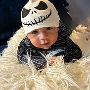 George is registered to the contest to win money with this photo: baby, infant, hat, skull_design, striped_clothing, blanket, fluffy, face, eyes, hands, bedroom, headboard, portrait, cute, child, smile, indoors, soft_texture, black_and_white, closeup