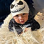 baby, infant, hat, skull_design, striped_clothing, blanket, fluffy, face, eyes, hands, bedroom, headboard, portrait, cute, child, smile, indoors, soft_texture, black_and_white, closeup