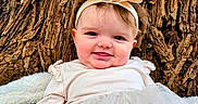 Eleanor is registered to the contest to win money with this photo: baby, child, smiling, headband, dress, tree_trunk, outdoor, nature, cute, portrait, infant, happy, face, skin, person, tulle, fabric, texture, young, closeup