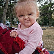 Eleanor is registered to the contest to win money with this photo: toddler, child, outdoor, blanket, pink_clothing, expression, face, hair, trees, nature, park, person, cute, cold_weather, holding, red, white, patterned_blanket, funny_face, portrait