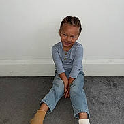Karnelo is registered to the contest to win money with this photo: braids, carpet, casual_clothing, child, cute, floor, happy, home, indoor, jeans, long_sleeve_shirt, mismatched_socks, person, playful, portrait, sitting, smile, socks, wall, young