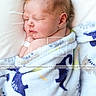 newborn, baby, sleeping, blanket, dinosaur_pattern, pillow, hospital_bracelet, infant, soft_texture, peaceful, cute, child, wrapped, portrait, closeup, bed, resting, skin, face, indoors
