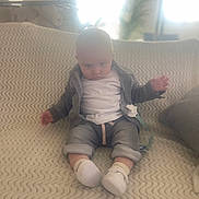 Aylan a rejoint le concours — aidez-le/la à gagner de superbes lots ! baby, child, clothing, couch, expression, furniture, gray_jacket, home, indoor, natural_light, pacifier, pants, patterned_blanket, person, portrait, seated, shoes, socks, soft_light, white_shirt