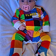 Erin is registered to the contest to win money with this photo: baby, pacifier, colorful_clothing, hat, infant, blanket, lying_down, indoors, cute, patchwork, soft, child, person, cozy, wearing, footed_pajamas, headwear, expression, comfort, young
