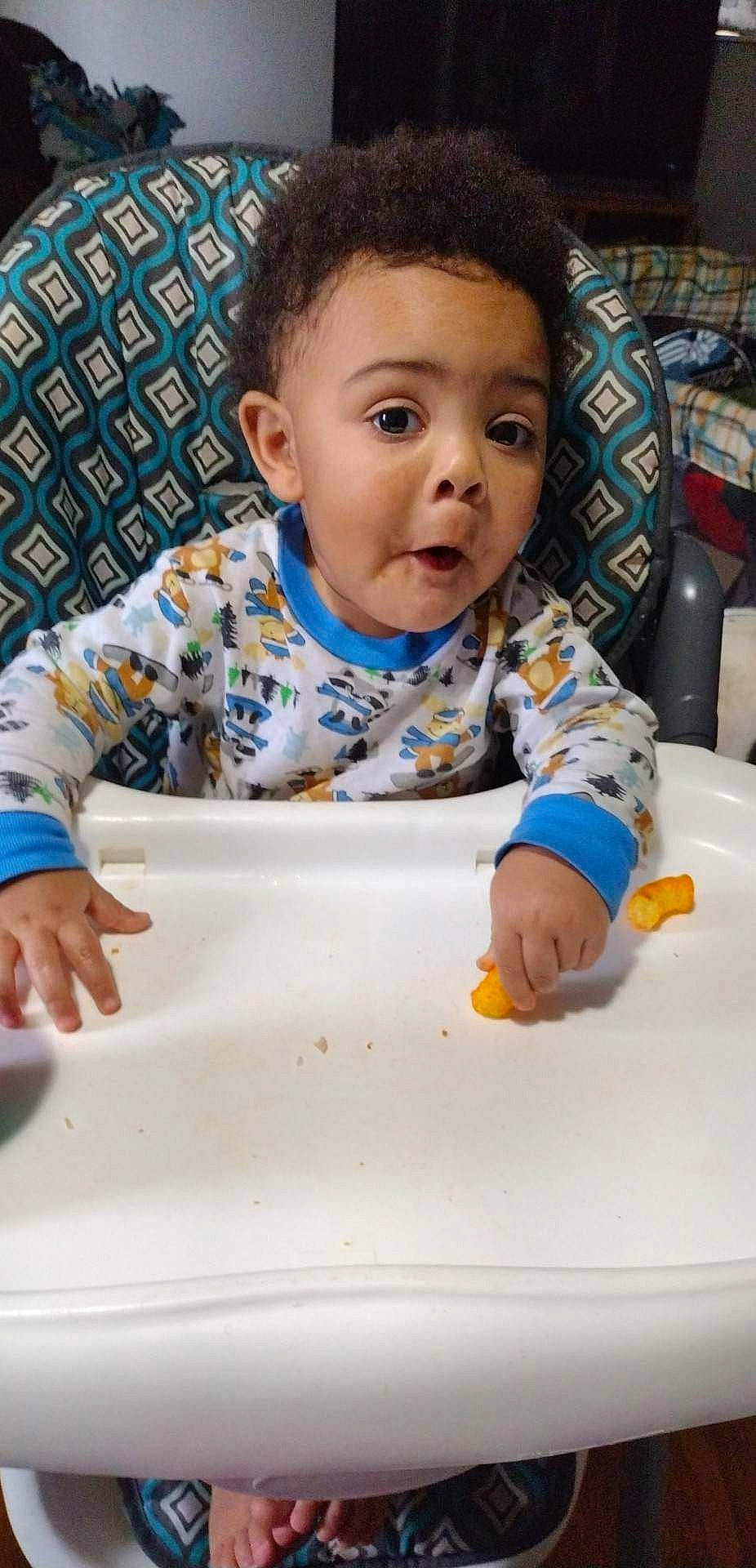 Julius is registered to the contest to win money with this photo: baby, baby_toddler_clothing, bib, chair, cheek, child, comfort_food, dishware, face, fun, happy, head, person, plate, product, room, serveware, sitting, sleeve, surprise