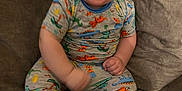 Easton joined the competition — help win amazing prizes! baby, child, smiling, laughing, pajamas, dinosaur_print, couch, indoor, happy, person, sitting, cute, infant, cozy, comfortable, clothing, living_room, young, portrait, playful