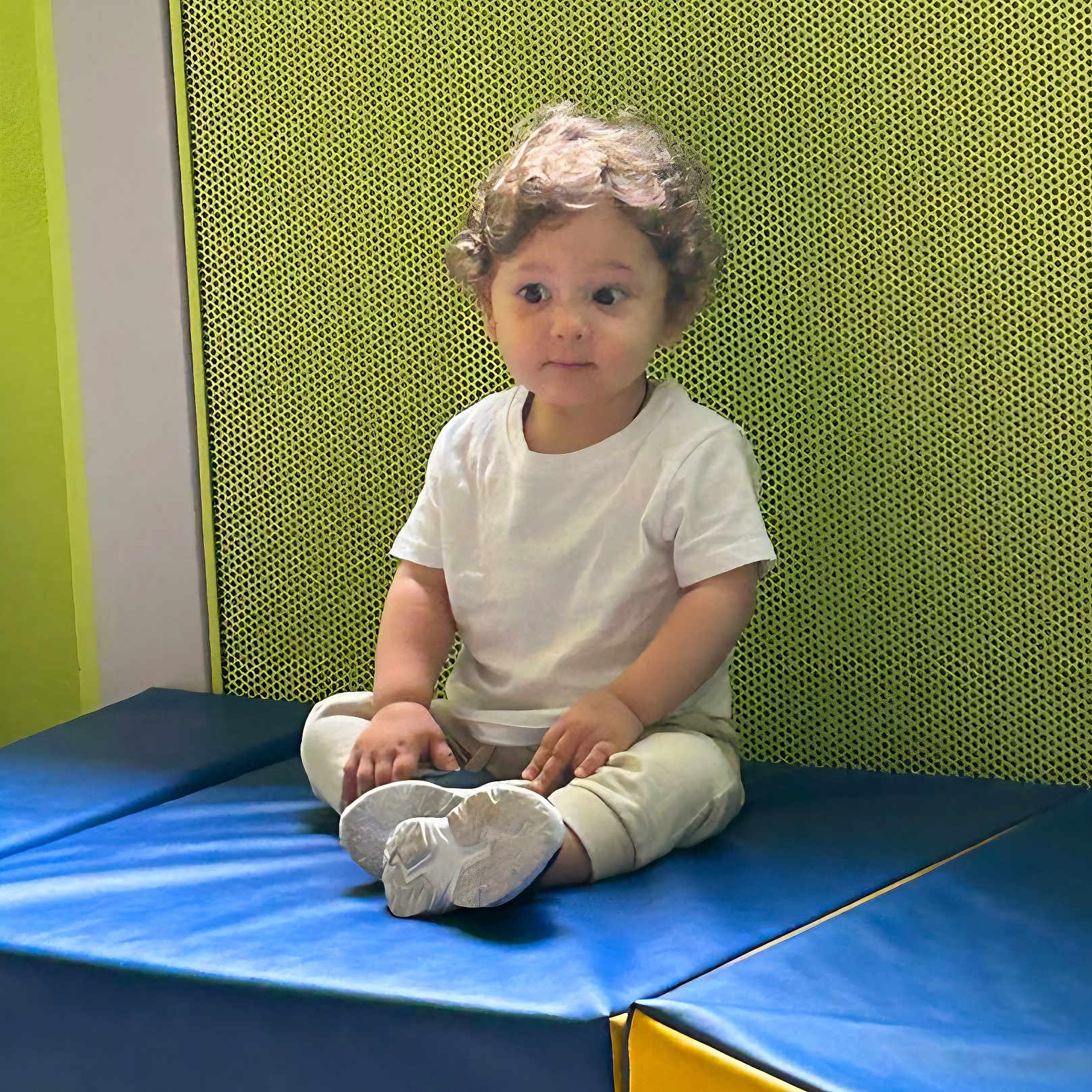 Daniel participe au concours pour gagner de l'argent avec cette photo : blue_mat, casual_clothing, child, cross_legged, curly_hair, cute, footwear, green_wall, indoor, looking_away, mat, pants, person, play_area, sitting, textured_wall, toddler, white_tshirt, yellow_mat, young_child