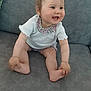 baby, child, smiling, pigtails, white_top, floral_collar, shorts, couch, gray_couch, indoor, happy, sitting, cute, hands, feet, skin, face, person, infant, tooth