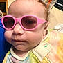 baby, child, sunglasses, pink_sunglasses, face, head, clothing, onesie, tie_dye, indoor, table, cup, dunkin, button, person, portrait, close_up, infant, casual, colorful