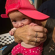 Serenity is registered to the contest to win money with this photo: baby, child, pink_cap, hand, polka_dot_pants, indoor, laundry_basket, adult_hand, rings, cross_necklace, cute, playful, person, clothing, face, expression, casual, holding, infant, headwear