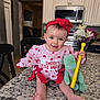 baby, infant, child, headband, red_bow, valentine_outfit, heart_pattern, smile, sitting, countertop, granite_counter, kitchen, microwave, cabinets, plush_toy, green_toy, yellow_stick, flowers, bouquet, bare_feet