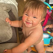 Ruby is registered to the contest to win money with this photo: baby, toddler, smiling, indoor, living_room, couch, toy, playtime, child, diaper, barefoot, floor, carpet, furniture, happy, cute, person, hand, foot, play