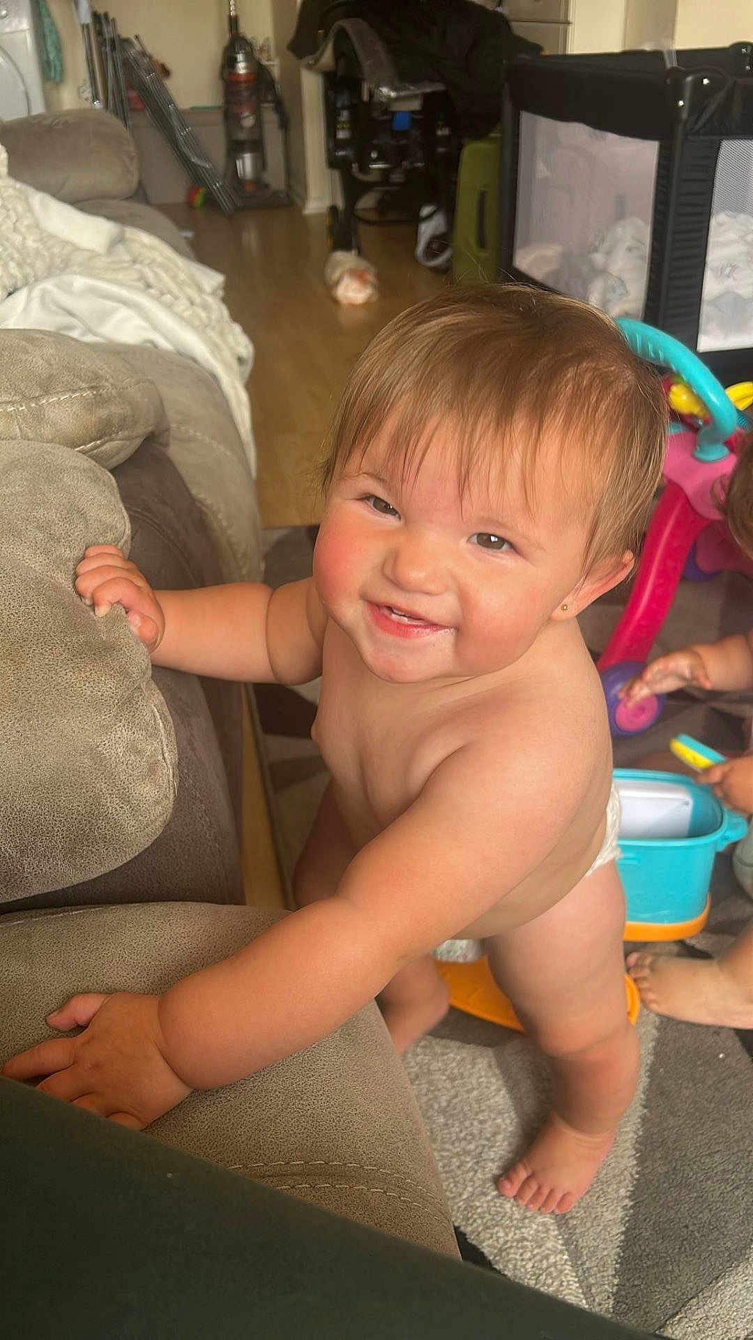 Ruby is registered to the contest to win money with this photo: baby, toddler, smiling, indoor, living_room, couch, toy, playtime, child, diaper, barefoot, floor, carpet, furniture, happy, cute, person, hand, foot, play