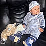baby, black_couch, blue_outfit, child, clothing, cute, footwear, giraffe, hand, indoor, infant, leather_couch, looking_away, plush_toy, portrait, relaxed, seated, sneakers, soft_toy, striped_hat