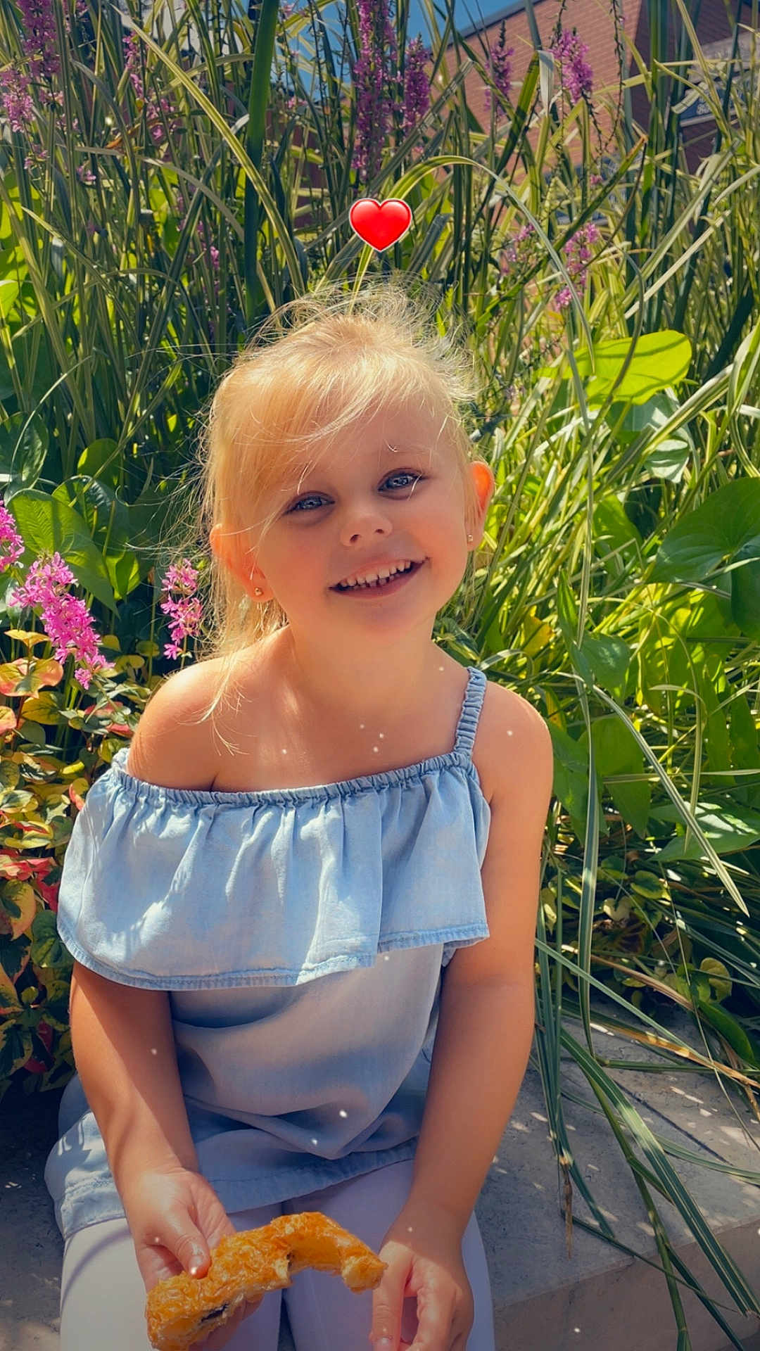 Molly participe au concours pour gagner de l'argent avec cette photo : child, girl, smiling, portrait, outdoor, garden, plants, flowers, greenery, blonde_hair, blue_dress, sitting, pastry, croissant, heart_sticker, sunlight, happy, eating, summer, casual_clothing