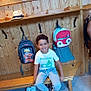 child, boy, smile, bench, backpack, wooden_wall, wooden_bench, shoes, casual_clothing, curly_hair, indoor, tile_floor, hooks, seat, happy, white_tshirt, blue_jeans, playful, school_bag, portrait