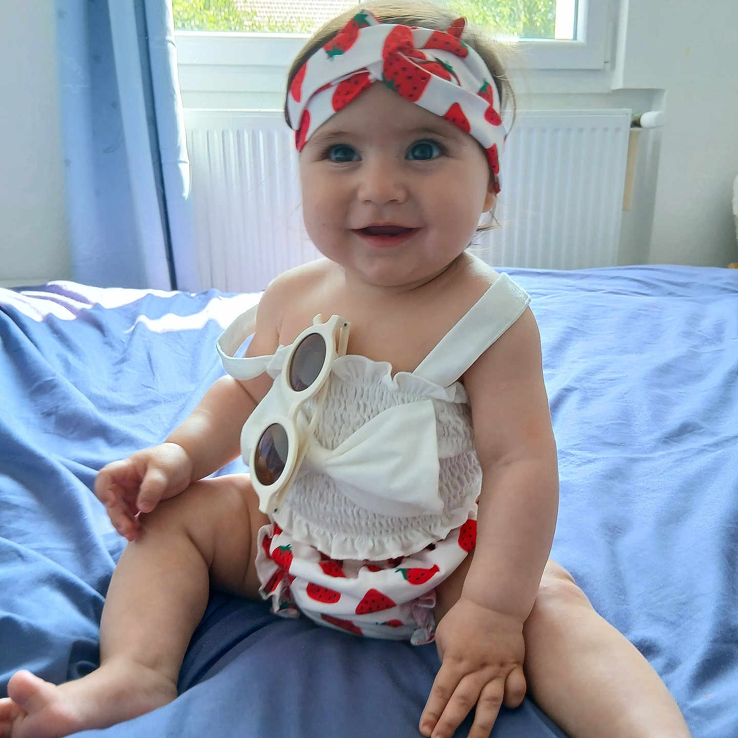 Melis a rejoint le concours — aidez-le/la à gagner de superbes lots ! baby, bed, blue_bedspread, child, clothing, cute, face, greenery, happy, headband, indoors, infant, person, playful, portrait, sitting, skin, smiling, sunglasses, window